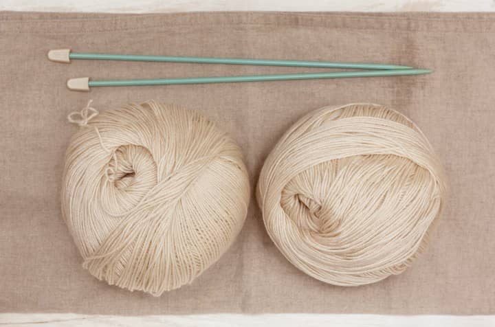 wo Balls of Cream Colored Cashmere Wool with straight knitting needles. 