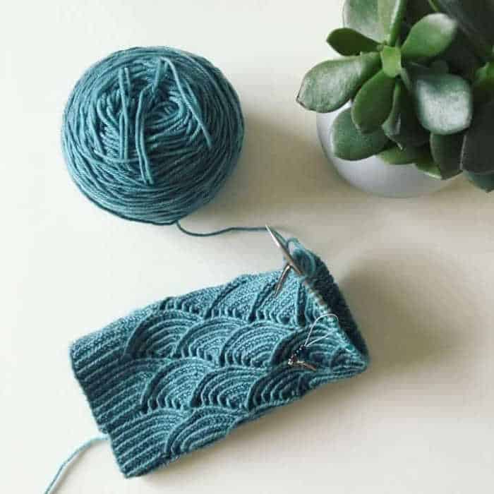 Socks on knitting needles in scallop pattern in teal blue yarn