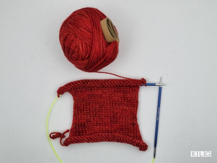 Swatch of stockinette knitting in red yarn unblocked with curling edges