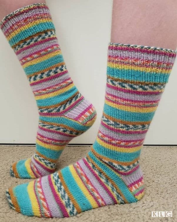 Knitted socks using Regia yarn that look like they use colorwork techniques. it is just how the yarn is dyed to make it look like patterns. Colors are turquoise, yellow, pink, white, green, orange and grey
