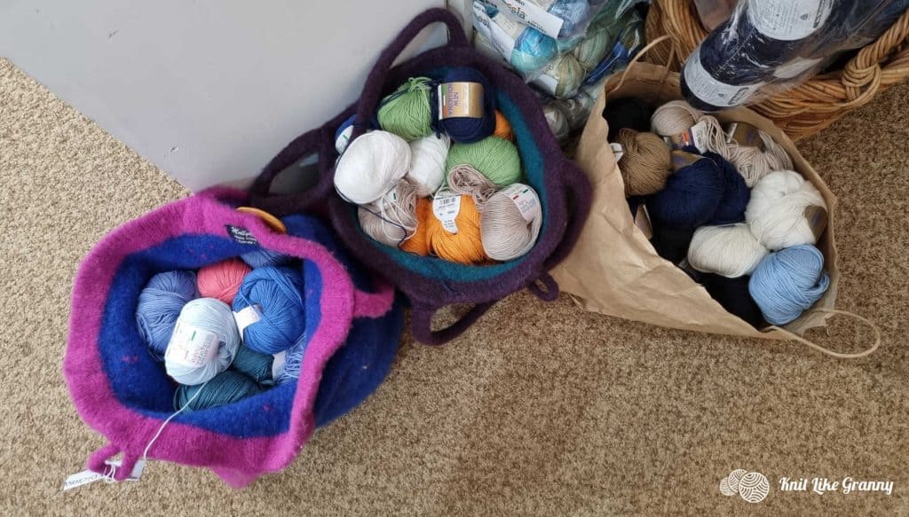 Bags full of yarn balls in different colors on a carpeted floor.